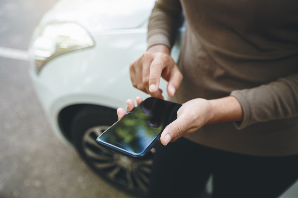 Person checking insurance telematics app on phone next to car